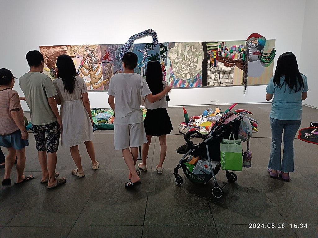 Obiskovalci v maju 2024 v Shenzhen Art Museum uporabljajo pametne telefone pred razstavnimi eksponati.